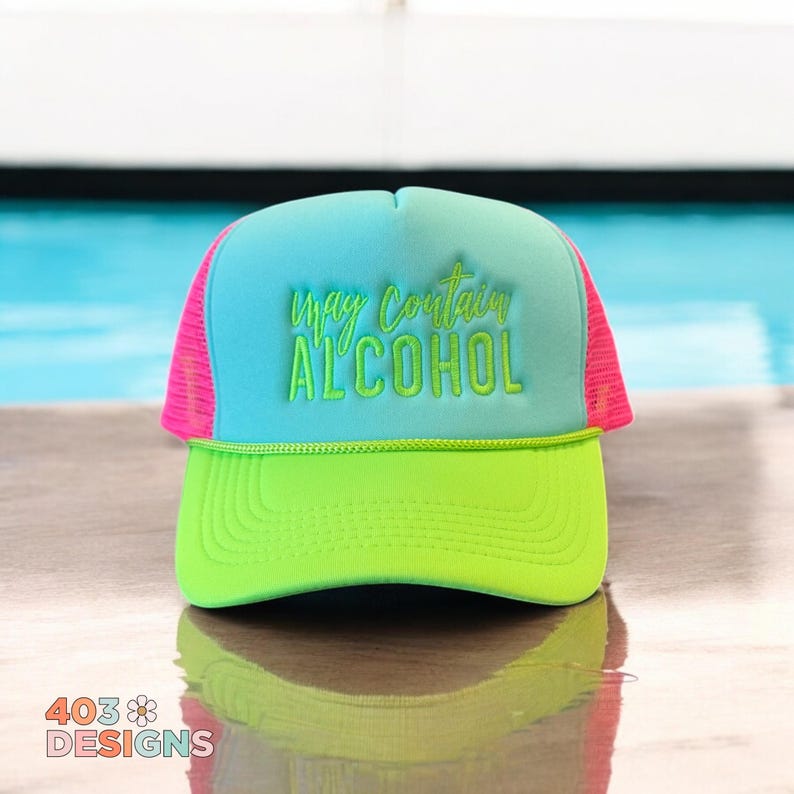 May include: A neon green and blue trucker hat with the text "may contain ALCOHOL" in green. The hat has a pink mesh back and a green brim. The hat is sitting on a wooden surface.