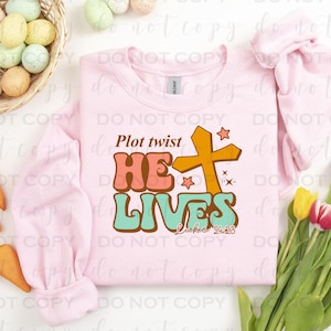 May include: Pink sweatshirt with a graphic design that says "Plot twist He Lives" in a retro font with a yellow cross and stars. The text "Luke 24:5" is also included in the design.