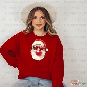 May include: A red sweatshirt with a graphic of Santa Claus wearing heart-shaped sunglasses and blowing a bubble. The Santa graphic is in a watercolor style.