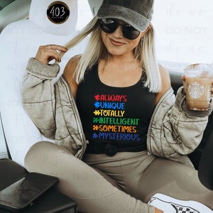 May include: A woman wearing a black tank top with the text "#ALWAYS #UNIQUE #TOTALLY #INTELLIGENT #SOMETIMES #MYSTERIOUS" in rainbow colors. She is sitting in a car and holding a cup of coffee.