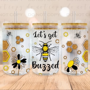 May include: Three clear glass tumblers with bamboo lids and straws. The tumblers have a gold glitter honeycomb pattern, a black and white daisy, and a bee with the text "Let's get buzzed".