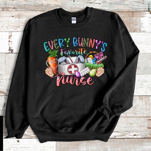 May include: Black sweatshirt with a colorful graphic of a bunny holding a first aid kit and other Easter-themed items. The text "Every Bunny's Favorite Nurse" is printed on the shirt.