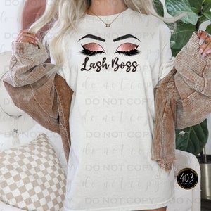 May include: White t-shirt with a graphic of two closed eyes with long eyelashes and glitter. The text "Lash Boss" is below the eyes.