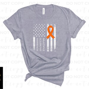 May include: A heather grey t-shirt with a white distressed American flag design. The flag has an orange ribbon in the center with the text "Multiple Sclerosis Awareness" printed vertically on the left side of the flag.