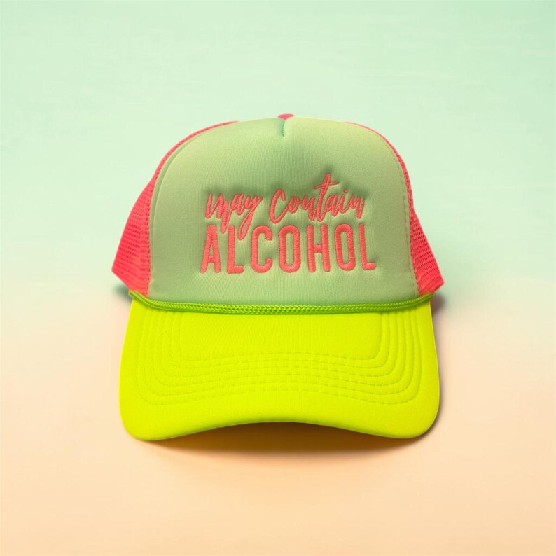 May include: A neon yellow and green trucker hat with a pink mesh back and brim. The hat features the embroidered text "may contain ALCOHOL" in pink, making it a fun and eye-catching accessory.