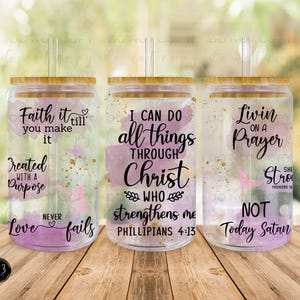May include: Three clear plastic tumblers with lids and straws. Each tumbler has a different inspirational quote printed on it. The quotes are "Faith it till you make it. Created with a purpose. Love never fails", "I can do all things through Christ who strengthens me. Philippians 4:13", and "Livin on a prayer. She is strong. Proverbs 31. Not today Satan."
