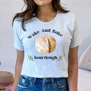 May include: A gray t-shirt with the text "Wake And Bake Sourdough" and a watercolor illustration of a sourdough bread loaf.