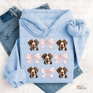 May include: A light blue hoodie with a pattern of brown and white dog faces and pink bows.