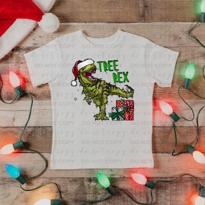May include: White t-shirt with a green dinosaur wearing a Santa hat and holding a Christmas present. The dinosaur is surrounded by green Christmas tree branches. The text "TREE REX" is printed on the shirt.