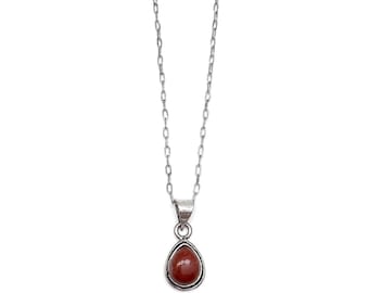 May include: A silver necklace with a teardrop-shaped pendant. The pendant features a reddish-brown stone set in a silver bezel. The chain is a delicate link style, and the necklace is displayed against a white background.