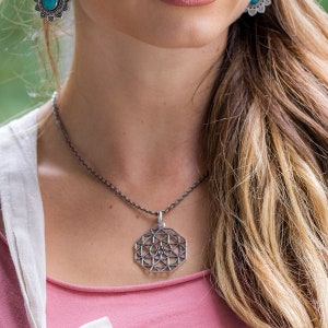 Op de afbeelding: Een zilveren ketting met een geometrische hanger. De hanger is een grote, achthoekige vorm met een gedetailleerd, ingewikkeld ontwerp.