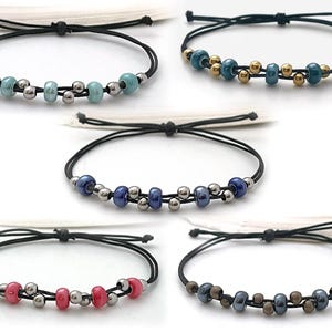 May include: Five adjustable bracelets with black cords. Each bracelet features a different color scheme of beads, including light blue, dark blue, red, and brown, interspersed with silver-colored beads. The bracelets are displayed against a white background.