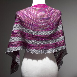 May include: A gray and pink knitted shawl with a lacy pattern. The shawl is draped over a white mannequin.