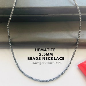 May include: A black hematite bead necklace with 2.5mm beads. The necklace is on a black surface. HEMATITE 2.5MM BEADS NECKLACE Starlight Gems Hub