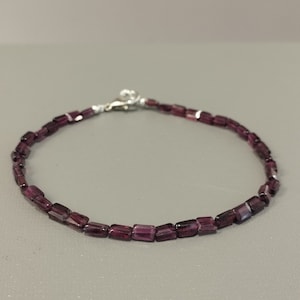 May include: A delicate bracelet made with small, rectangular, purple gemstones. The bracelet has a silver clasp.