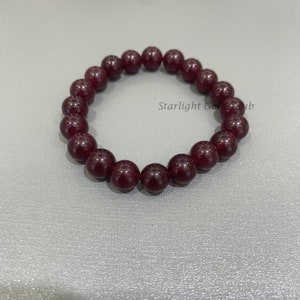 May include: A dark red gemstone bracelet with round beads. The bracelet is made of natural stones and is approximately 7 inches in length.