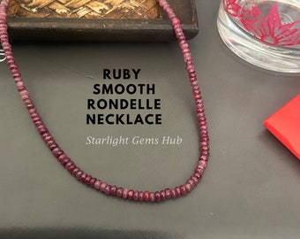 Może przedstawiać: Naszyjnik z gładkich, okrągłych koralików z rubinu w kolorze czerwonym. Naszyjnik leży na ciemnej powierzchni z tekstem "RUBY SMOOTH RONDELE NECKLACE Starlight Gems Hub".