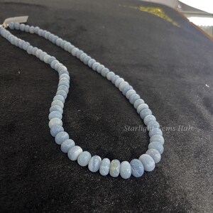 May include: A light blue gemstone necklace with round beads. The necklace is on a black surface with the text "Starlight Gems Hub".