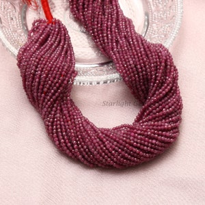 May include: A strand of ruby red faceted gemstone beads. The beads are small and round, and they are strung on a clear thread. The beads are arranged in a loose, flowing pattern.