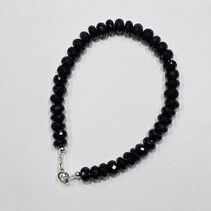 May include: A black beaded bracelet with a silver clasp. The bracelet features small, faceted black beads. The beads are strung together to form a continuous loop. The clasp is a simple, silver design, providing a secure closure for the bracelet.