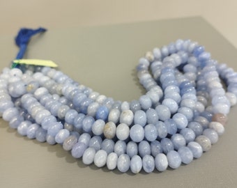 May include: A strand of light blue gemstone beads. The beads are round and smooth, and they have a slightly translucent appearance. The beads are strung on a thin cord, and they are arranged in a loose, flowing pattern.