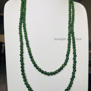 Puede incluir: Un collar largo de doble cadena hecho de cuentas de jade verde oscuro. El collar se muestra en un busto de maniqu&iacute; blanco.