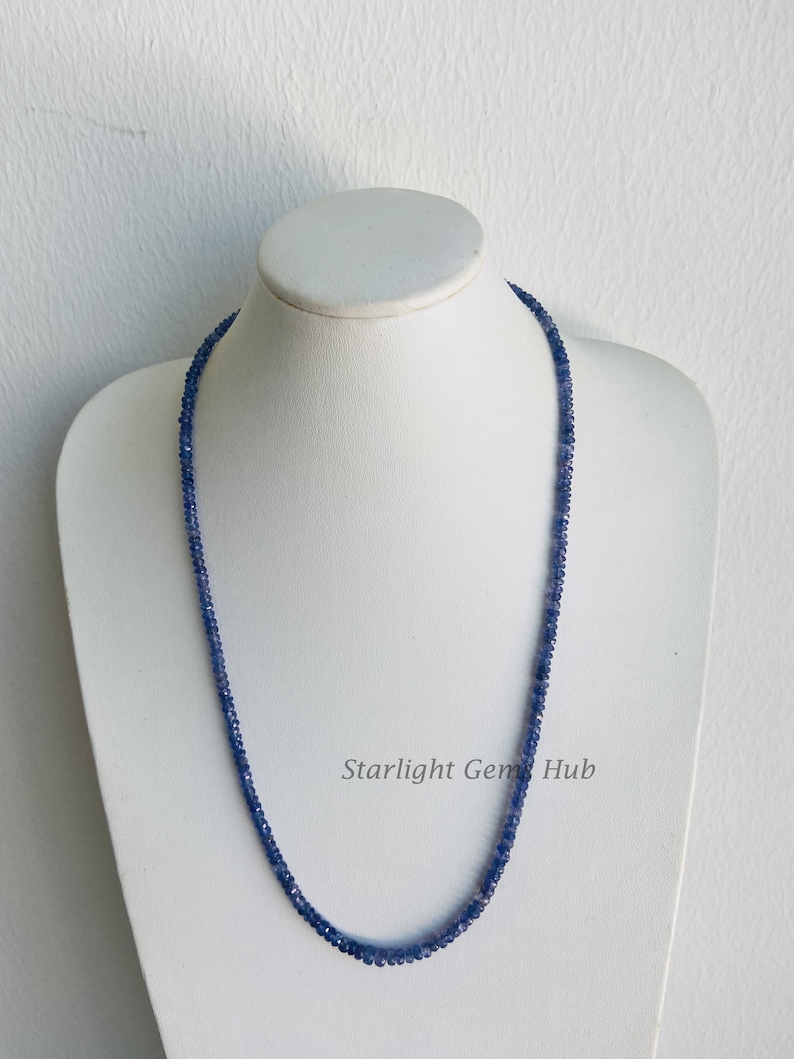 May include: A blue sapphire gemstone necklace on a white mannequin. The necklace is made of small, round beads and is approximately 18 inches long. The necklace is called "Starlight Gem Hub".