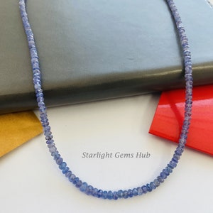 May include: A necklace made of small, light blue gemstone beads. The necklace is on a dark gray surface. The text "Starlight Gems Hub" is visible in the image.