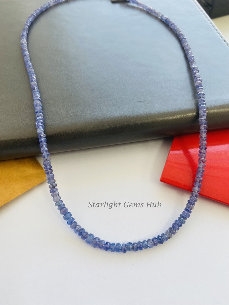 May include: A necklace made of small, light blue gemstone beads. The necklace is on a dark gray surface. The text "Starlight Gems Hub" is visible in the image.