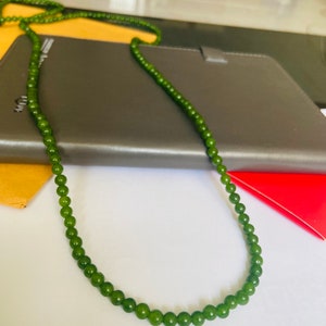 Puede incluir: Un collar de cuentas de jade verde con un dise&ntilde;o sencillo. El collar est&aacute; hecho de cuentas redondas y est&aacute; enhebrado en un cord&oacute;n delgado.