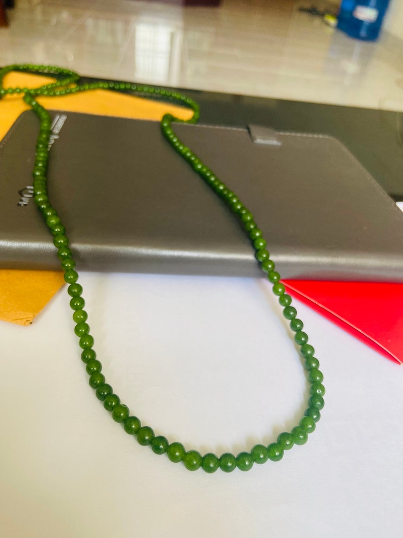 Puede incluir: Un collar de cuentas de jade verde con un dise&ntilde;o sencillo. El collar est&aacute; hecho de cuentas redondas y est&aacute; enhebrado en un cord&oacute;n delgado.