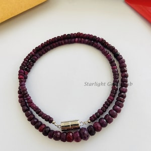 Pode incluir: Um colar de duas voltas feito de contas de pedras preciosas de cor púrpura escura com um fecho magnético. O colar está sobre uma superfície branca.  Starlight Gems Hub está impresso na superfície.