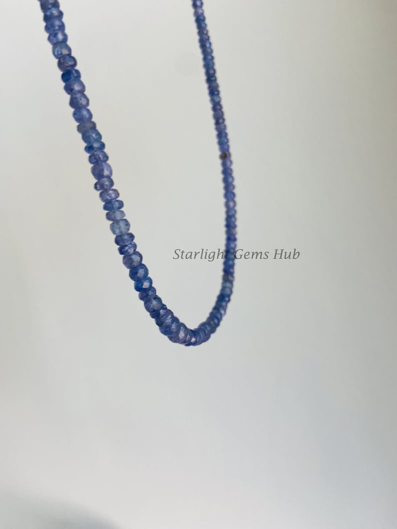 May include: A strand of light blue gemstone beads, strung on a thin wire. The beads are faceted and have a slightly irregular shape. The strand is hanging in a loop, with the ends of the wire visible.