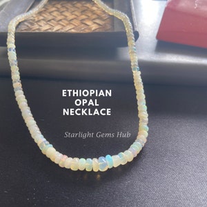 May include: A white opal necklace made of small, round beads. The necklace is on a black surface and the text "ETHIOPIAN OPAL NECKLACE" and "Starlight Gems Hub" is visible below the necklace.