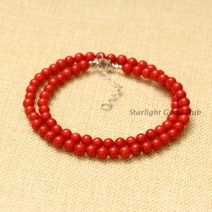 May include: A double strand necklace made of bright red coral beads with a silver clasp. The necklace is on a beige fabric background.