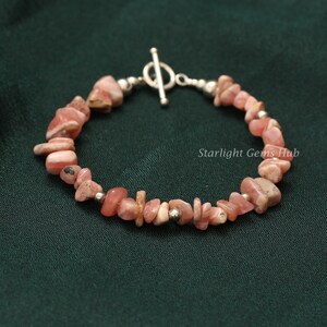 Op de afbeelding: Een roze en zilveren armband gemaakt van kleine, onregelmatig gevormde stenen. De armband heeft een zilveren schuifgesp.