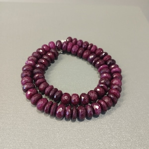Puede incluir: Un collar de cuentas de rubí rojo oscuro, enhebradas en un hilo de plata. Las cuentas son facetadas y tienen una forma ligeramente irregular.