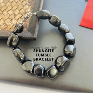 Könnte beinhalten: Schwarzes Shungit-Tumble-Armband mit silbernem Verschluss. Starlight Gems Hub Shungite Tumble Bracelet.