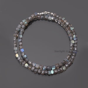 Puede incluir: Un collar de doble cadena hecho con cuentas de labradorita cuadradas, facetadas e iridiscentes. El collar mide aproximadamente 45 cm de largo y tiene un cierre de plata.