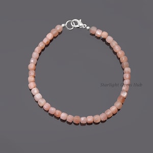 May include: A pink sunstone bracelet with a silver clasp. The bracelet is made of square-shaped beads.