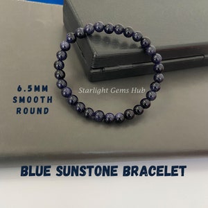 Puede incluir: Pulsera de piedra de sol azul con cuentas redondas lisas de 6,5 mm. La pulsera está hecha de piedra de sol azul con un acabado brillante. El texto "Starlight Gems Hub" es visible en la imagen.