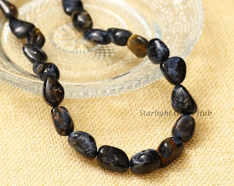 May include: A strand of dark blue and gold tiger's eye beads, with a smooth, rounded shape. The beads are strung on a clear cord and are arranged in a loose, flowing pattern.