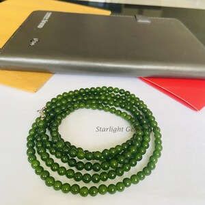 Puede incluir: Un collar de cuentas de jade verde con un cierre de plata. El collar est&aacute; hecho de m&uacute;ltiples hilos de cuentas y est&aacute; colocado sobre una superficie blanca.