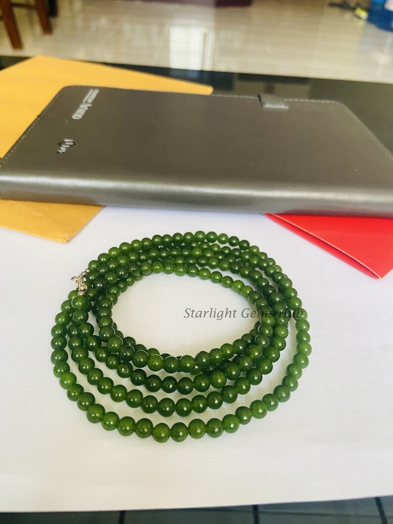 Puede incluir: Un collar de cuentas de jade verde con un cierre de plata. El collar est&aacute; hecho de m&uacute;ltiples hilos de cuentas y est&aacute; colocado sobre una superficie blanca.