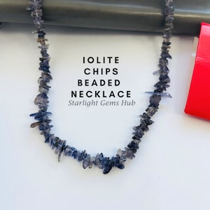 Puede incluir: Un collar hecho de virutas de iolite. El collar es azul y gris y tiene forma de viruta. El texto "Iolite Chips Beaded Necklace Starlight Gems Hub" está escrito debajo del collar.