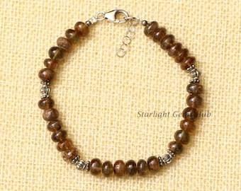May include: A brown gemstone beaded bracelet with silver accents and a silver clasp. The bracelet is on a beige fabric background.  Starlight Gems Hub is printed on the background.