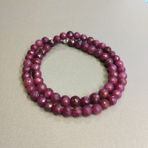 Op de afbeelding: Een ketting gemaakt van diep rode gefacetteerde edelsteen kralen. De kralen zijn rond en hebben een gepolijste afwerking.