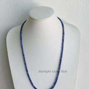 May include: A blue sapphire gemstone necklace on a white mannequin. The necklace is made of small, round beads and is approximately 18 inches long. The necklace is called "Starlight Gem Hub".