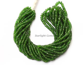 May include: A strand of green gemstone beads, likely peridot, with a faceted, slightly elongated shape. The beads are strung on a white thread and are arranged in a loose, flowing pattern.