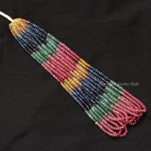 May include: A multi-coloured strand of gemstone beads. The beads are faceted and arranged in alternating rows of pink, green, blue, and yellow.